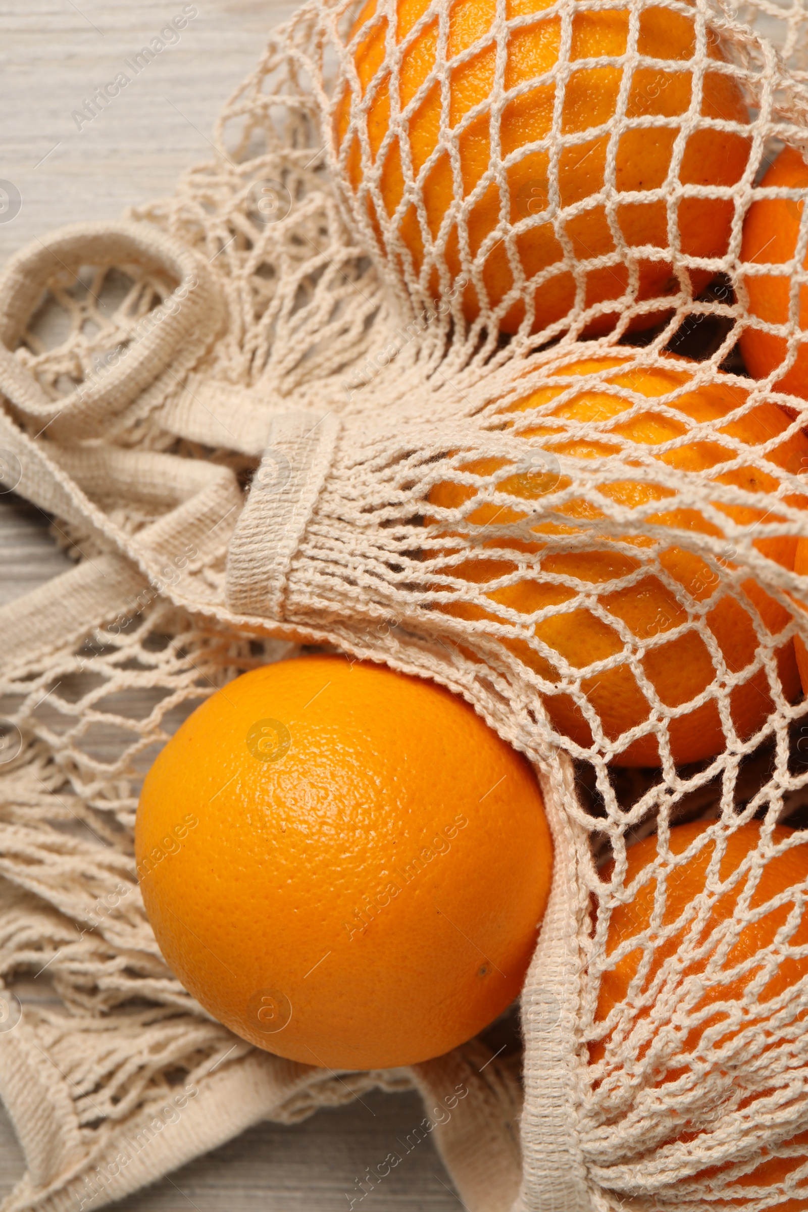 Photo of Many ripe juicy oranges with net bag on wooden table, closeup