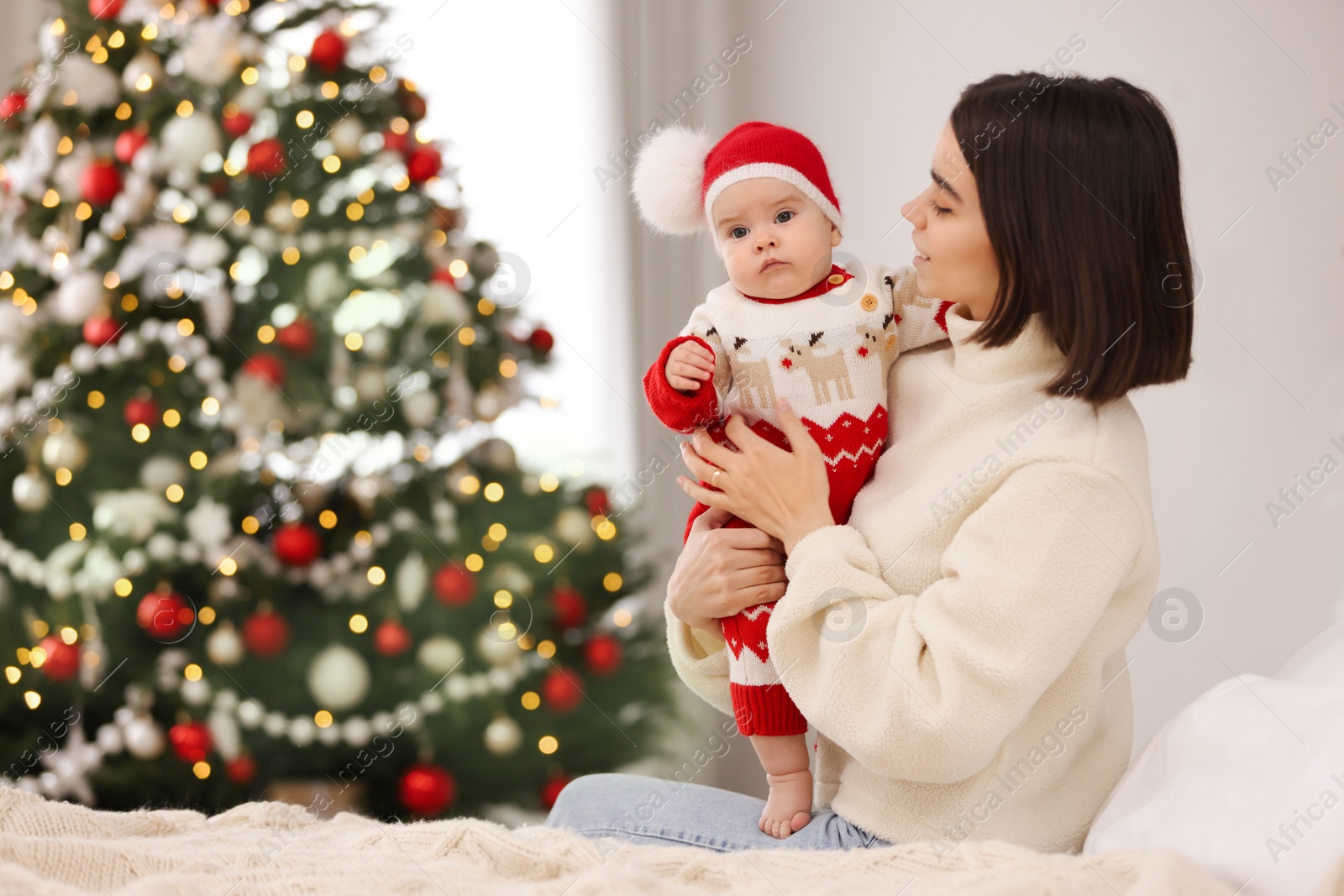 Photo of Happy young mother with her cute baby on bed, space for text. Winter holiday