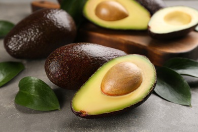 Whole and cut avocados with green leaves on grey table, closeup