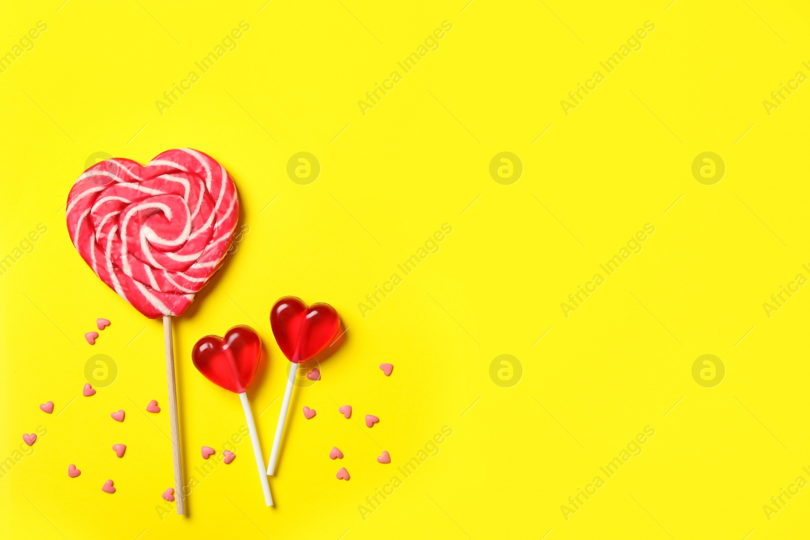 Photo of Sweet heart shaped lollipops and sprinkles on yellow background, flat lay with space for text. Valentine's day celebration