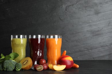 Photo of Delicious colorful juices in glasses and fresh ingredients on black table. Space for text