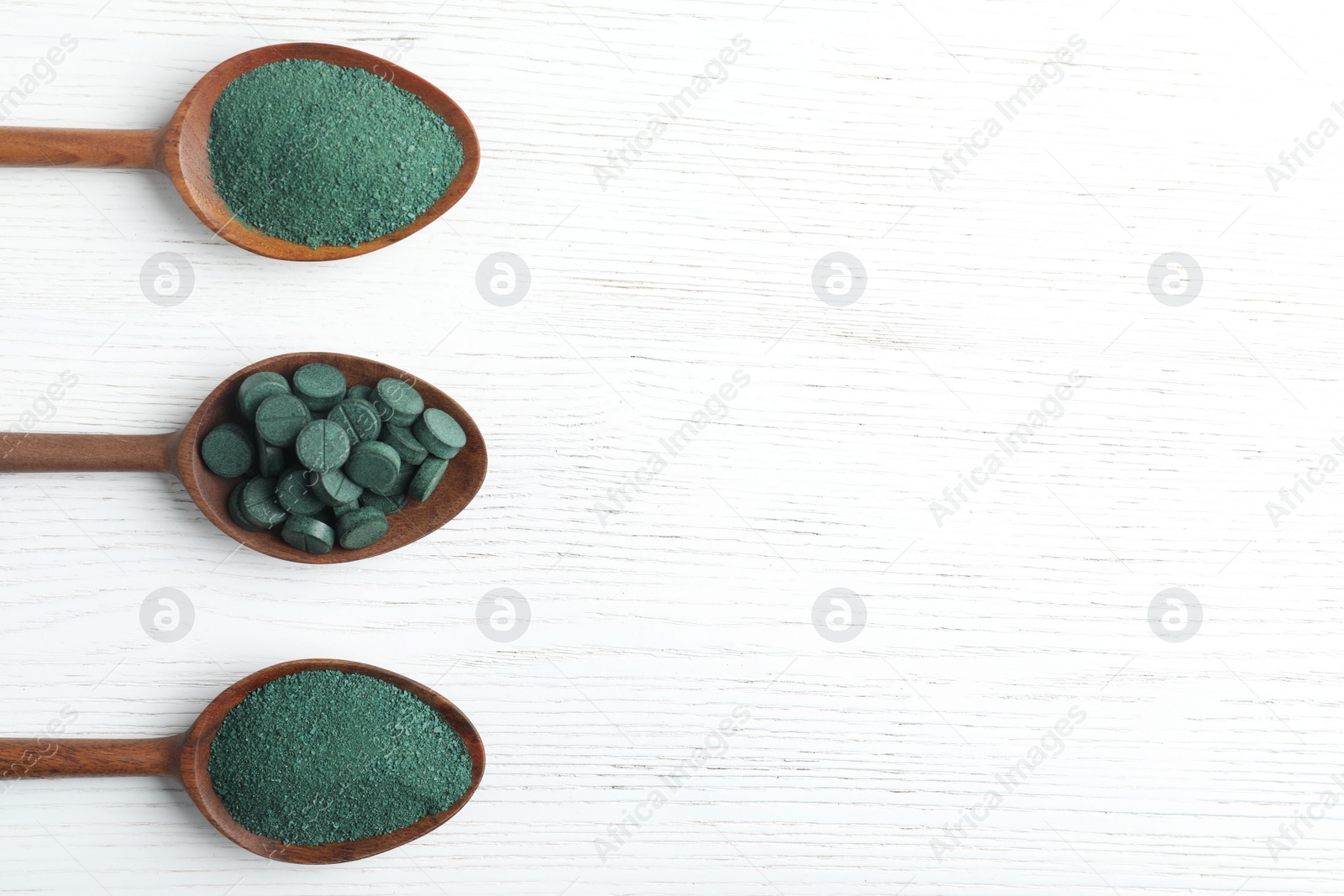 Photo of Spoons of spirulina powder and pills on white wooden background, top view with space for text