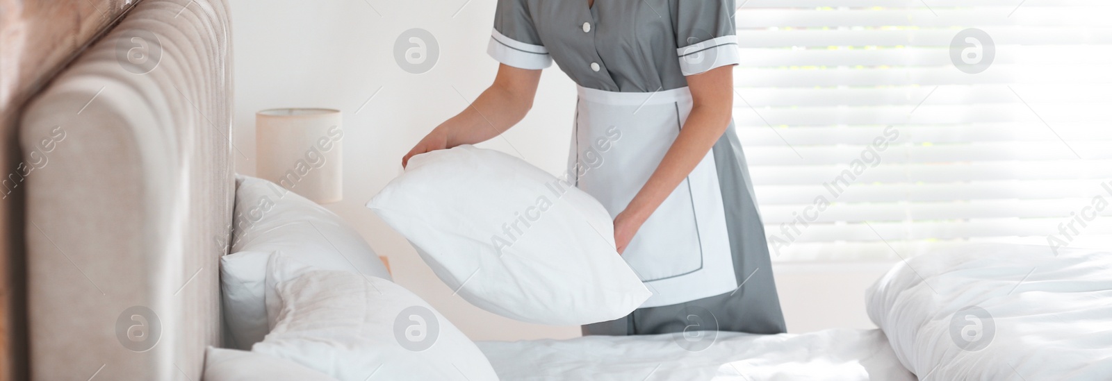 Image of Young chambermaid making bed in hotel room, closeup. Banner design