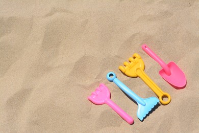 Photo of Bright plastic rakes and shovel on sand, space for text. Beach toys