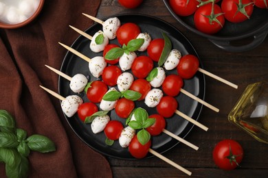Photo of Caprese skewers with tomatoes, mozzarella balls, basil and spices on wooden table, flat lay