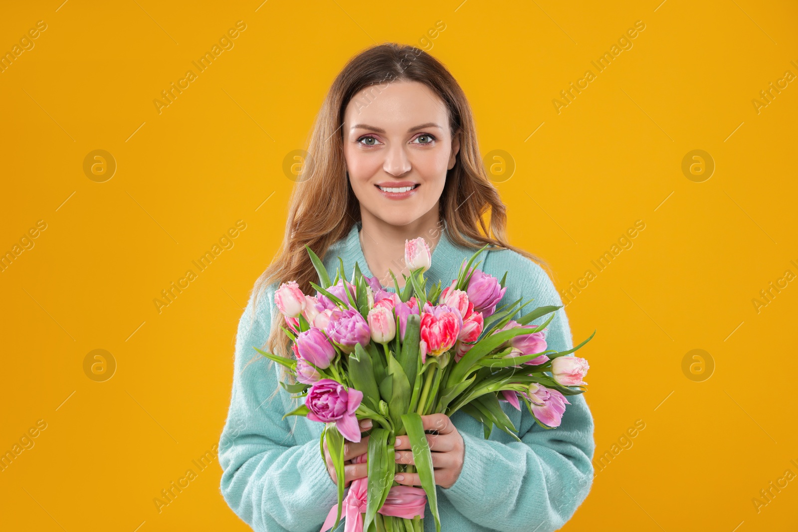 Photo of Happy young woman with bouquet of beautiful tulips on yellow background