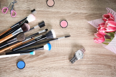 Flat lay composition with professional brushes, makeup products and tulips on wooden background