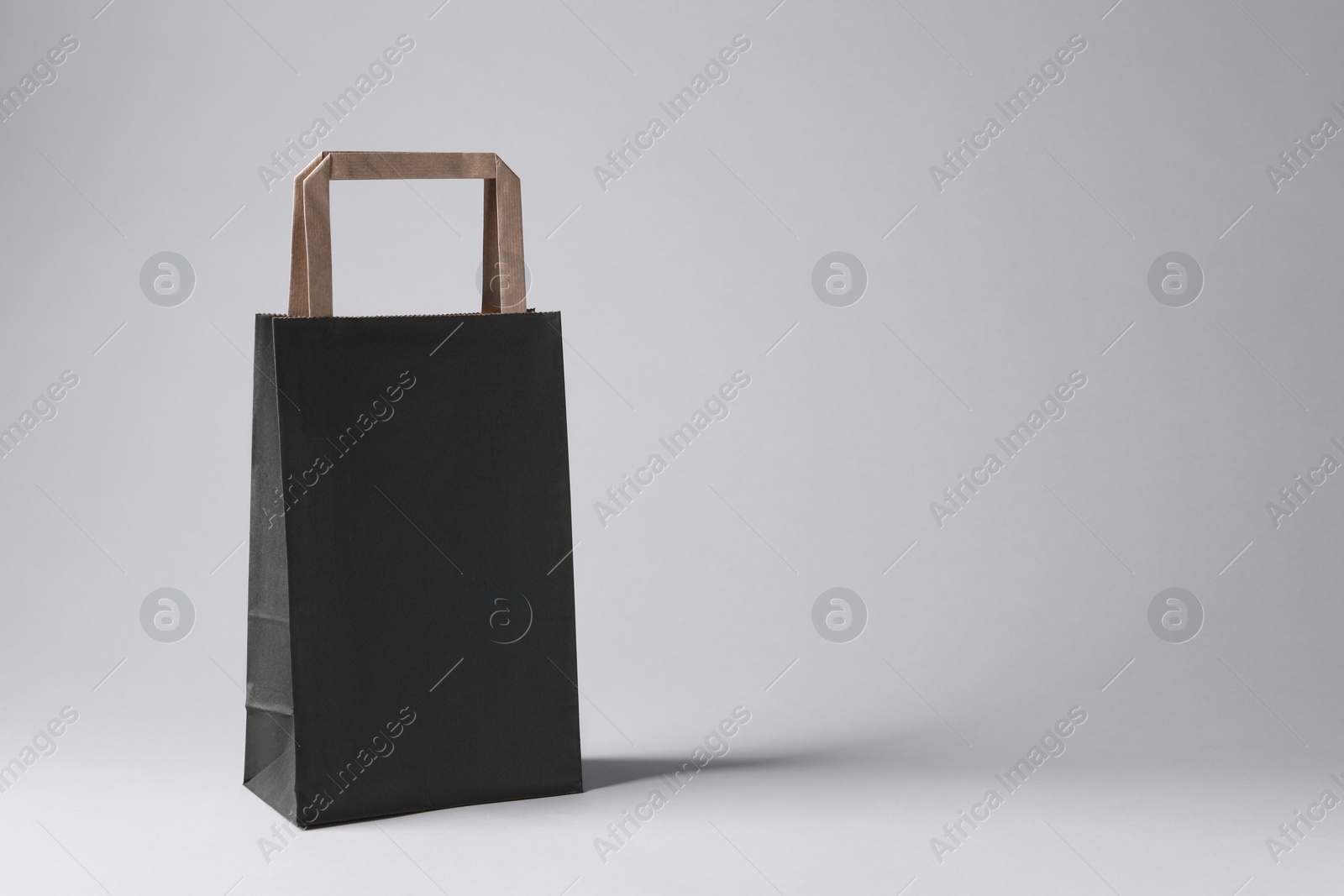 Photo of Black paper bag on light grey background, space for text