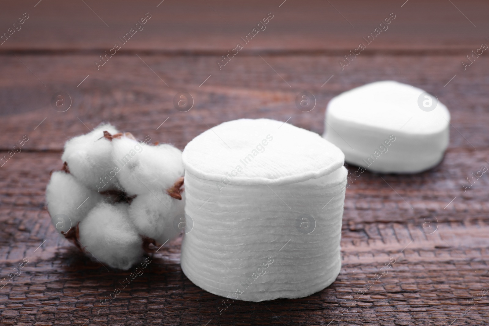 Photo of Stack of clean cotton pads and flower on wooden table, closeup