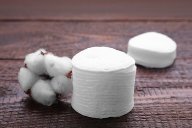 Stack of clean cotton pads and flower on wooden table, closeup