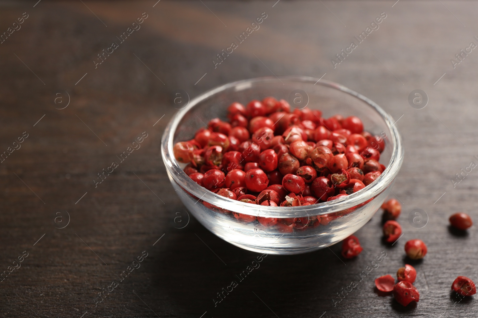 Photo of Glass bowl with red peppercorns on wooden table