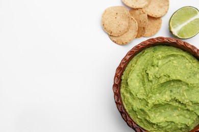 Photo of Delicious guacamole made of avocados, lime and chips on white background, flat lay. Space for text