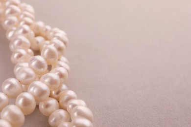 Elegant pearl necklace on beige background, closeup. Space for text