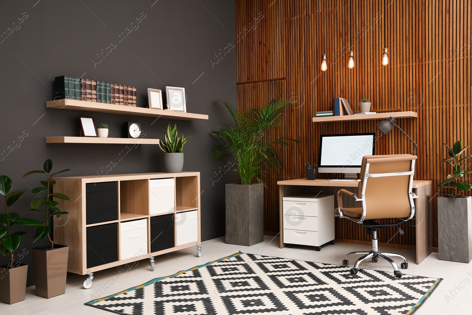 Photo of Comfortable workplace with computer near wooden wall in stylish room interior. Home office design