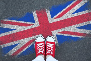 Image of Immigration. Woman standing on asphalt near flag of United Kingdom, top view