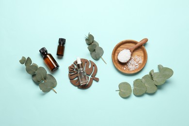 Photo of Aromatherapy products. Bottles of essential oil, sea salt and eucalyptus branches on light blue background, flat lay
