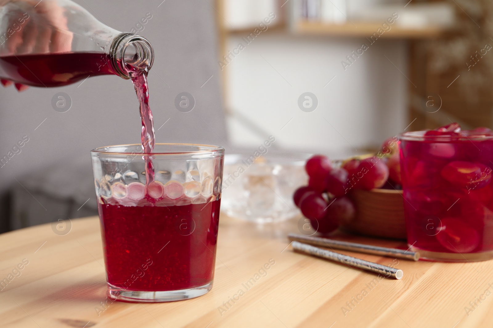 Photo of Woman pouring grape soda water into glass at wooden table indoors, closeup. Refreshing drink