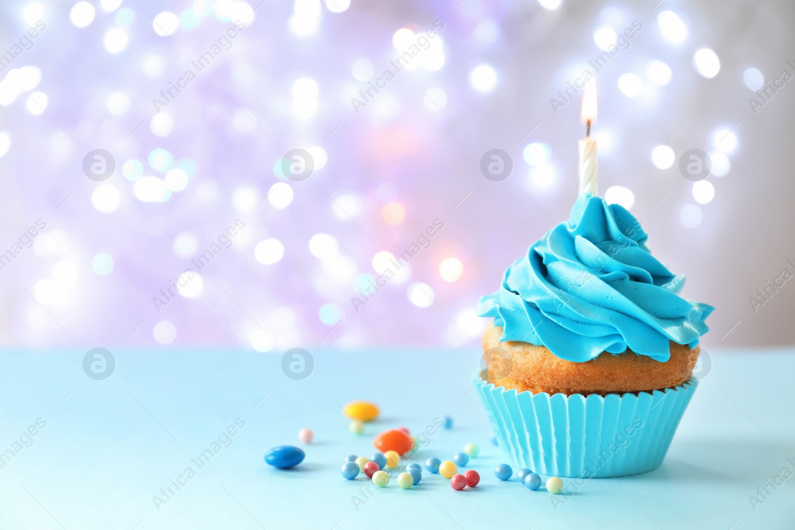 Photo of Delicious birthday cupcake with candle on table against blurred background