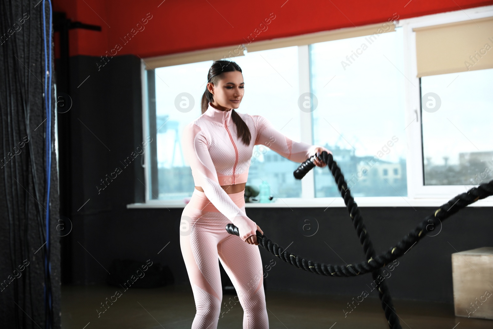 Photo of Young woman working out with battle ropes in modern gym