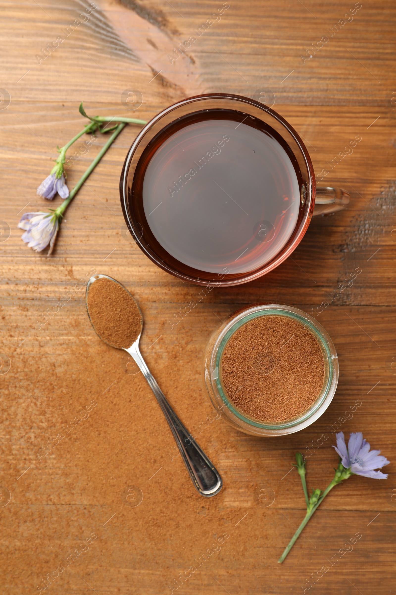 Photo of Cup of delicious chicory drink, powder and flowers on wooden table, flat lay