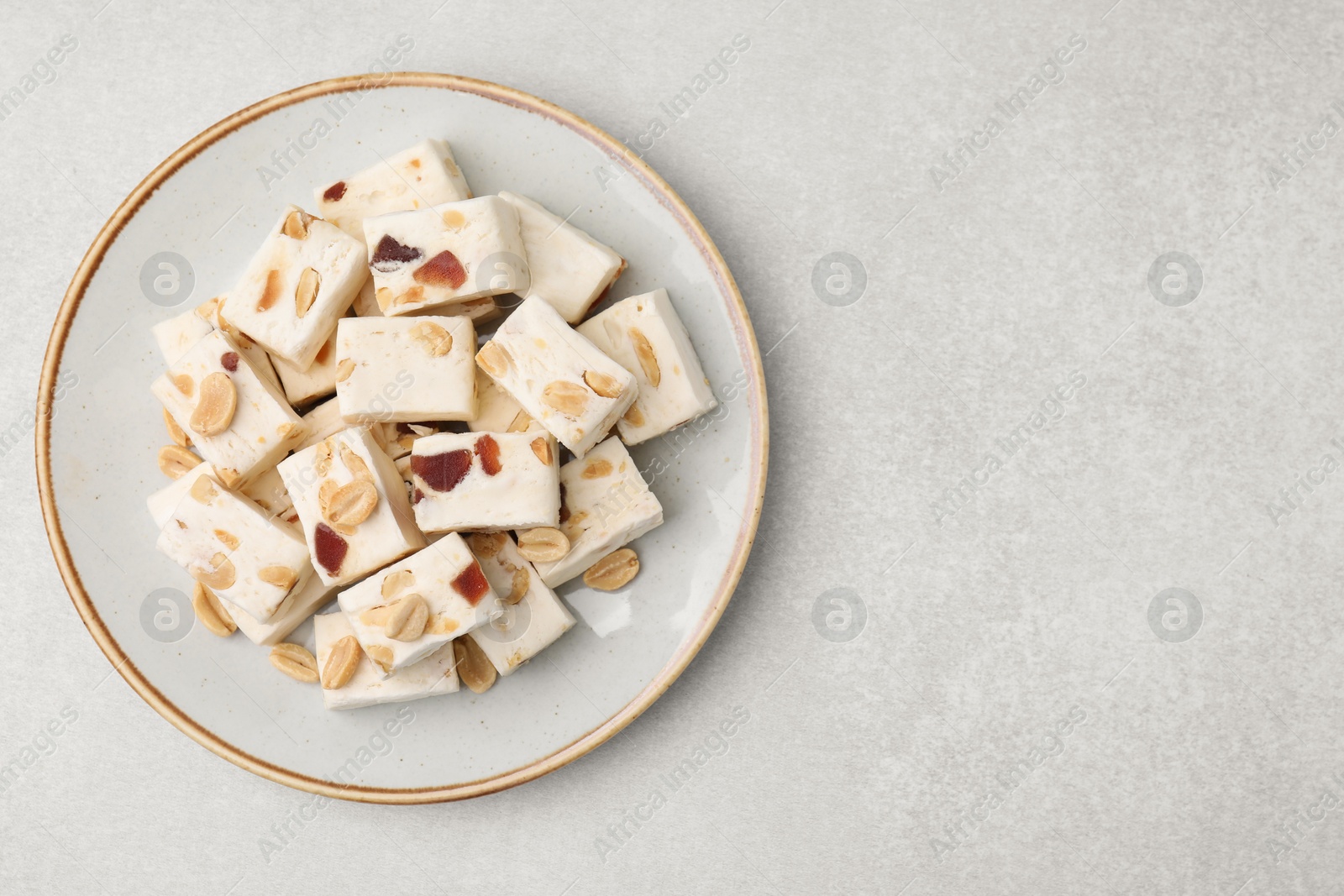 Photo of Pieces of delicious nutty nougat on light gray table, top view. Space for text