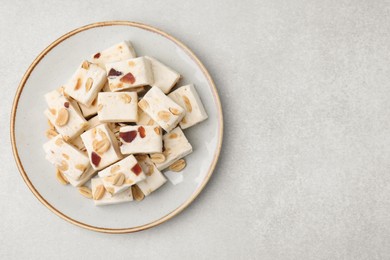 Photo of Pieces of delicious nutty nougat on light gray table, top view. Space for text