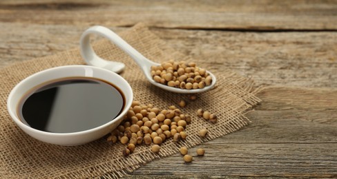 Photo of Soy sauce in bowl and beans on wooden table, closeup. Space for text