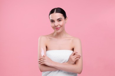 Photo of Beautiful woman with smear of body cream on her arm against pink background