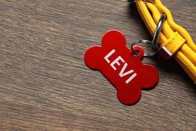 Image of Yellow leather dog collar with red tag in shape of bone on wooden table, top view. Space for text