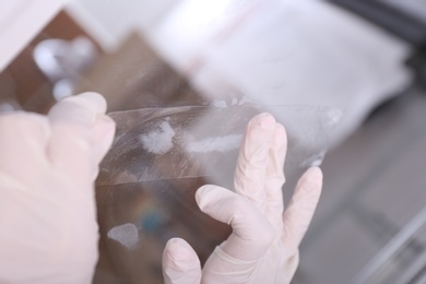 Photo of Detective using adhesive tape to take fingerprints from glass surface indoors, closeup