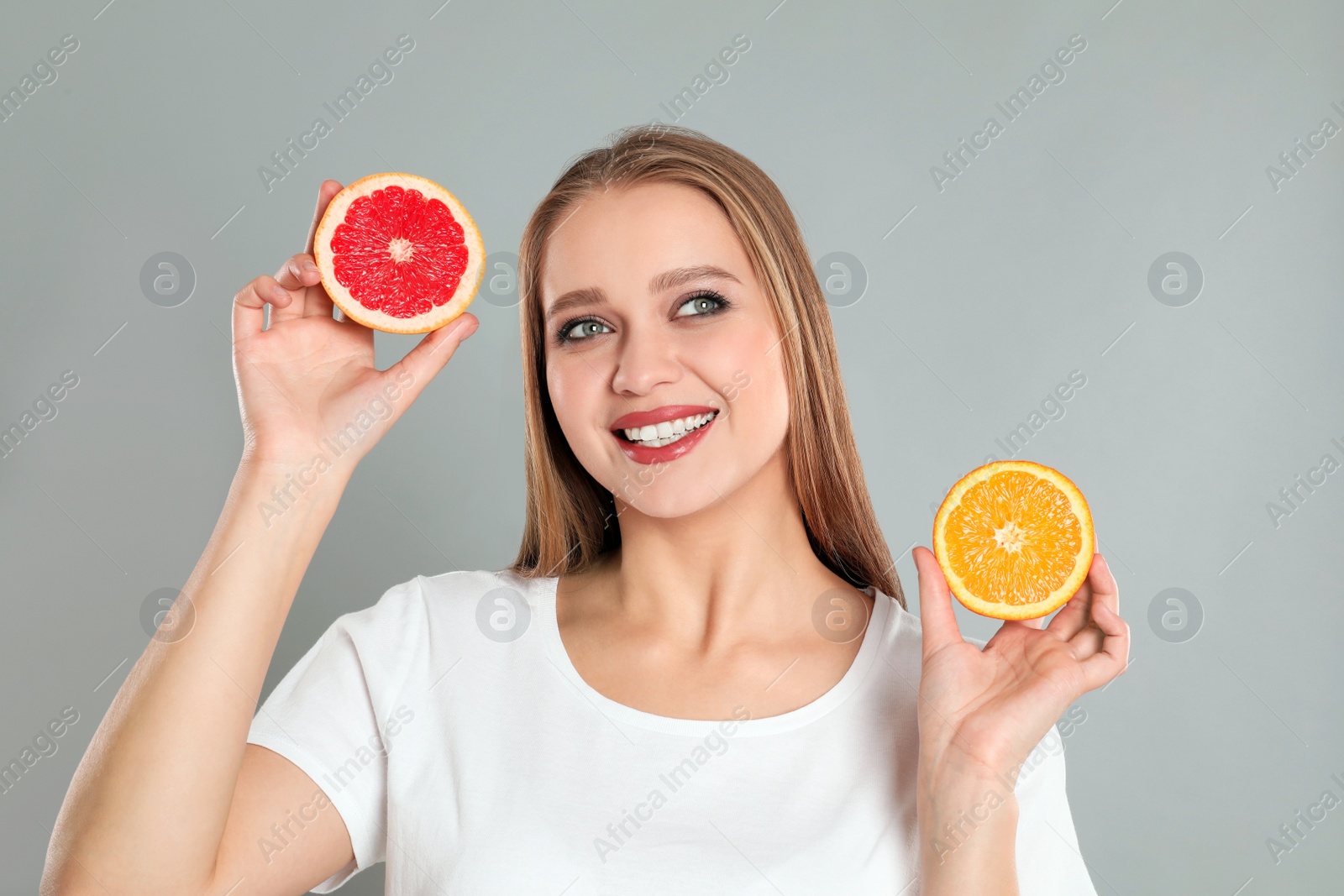 Photo of Young woman with cut orange and grapefruit on grey background. Vitamin rich food