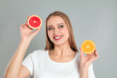 Photo of Young woman with cut orange and grapefruit on grey background. Vitamin rich food