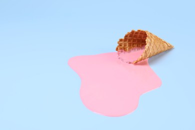 Photo of Melted ice cream and wafer cone on light blue background, space for text