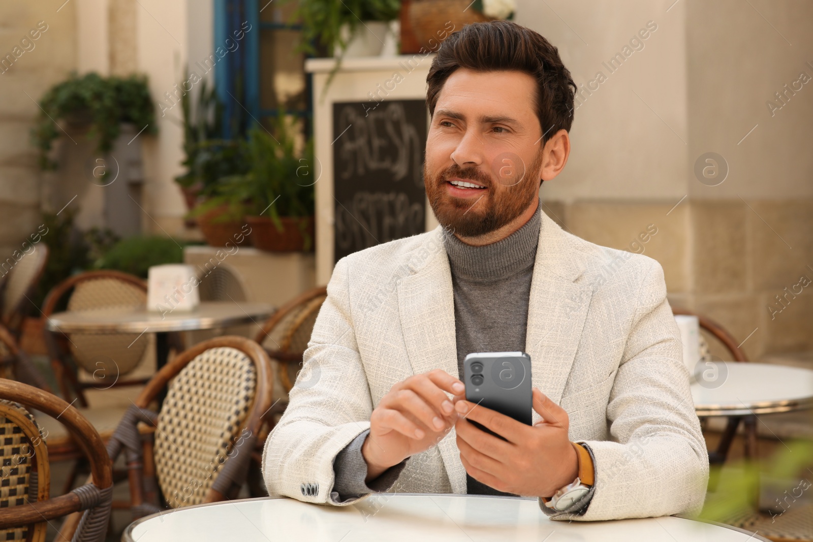 Photo of Handsome man with smartphone at table in outdoor cafe