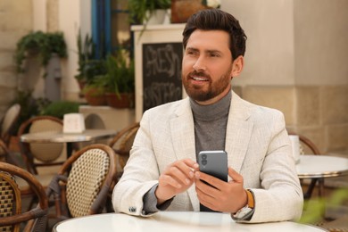 Photo of Handsome man with smartphone at table in outdoor cafe