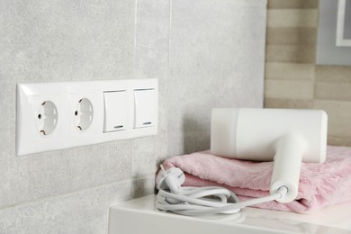 Power sockets, light switches on wall near table with hairdryer and towel indoors, space for text