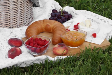 Photo of Picnic blanket with tasty food and basket on green grass outdoors