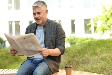 Photo of Handsome mature man with newspaper on bench in park. Space for text