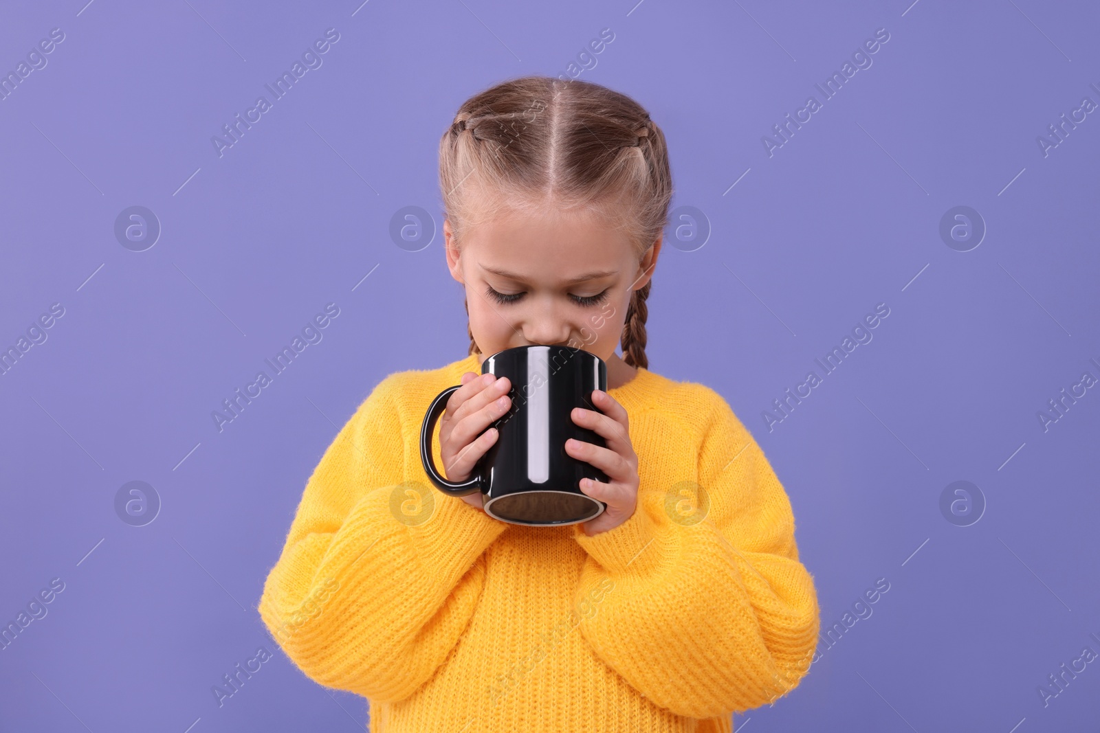 Photo of Cute girl drinking beverage from black ceramic mug on violet background