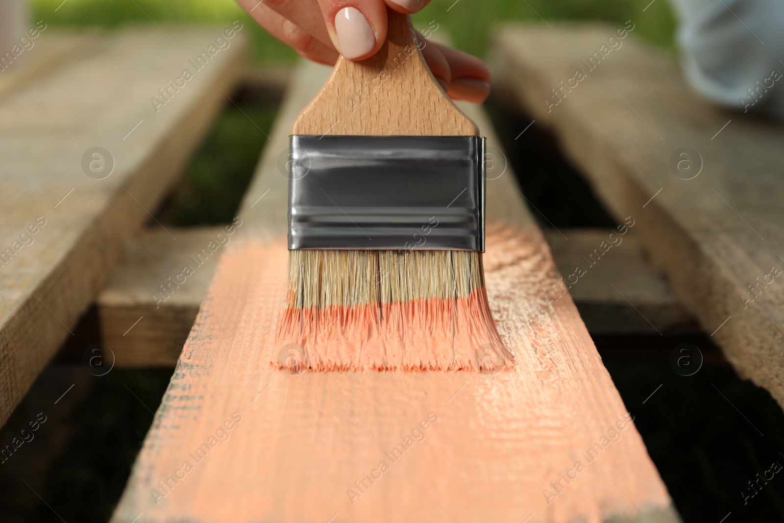 Photo of Woman painting wooden surface with coral dye outdoors, closeup