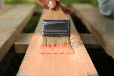 Photo of Woman painting wooden surface with coral dye outdoors, closeup