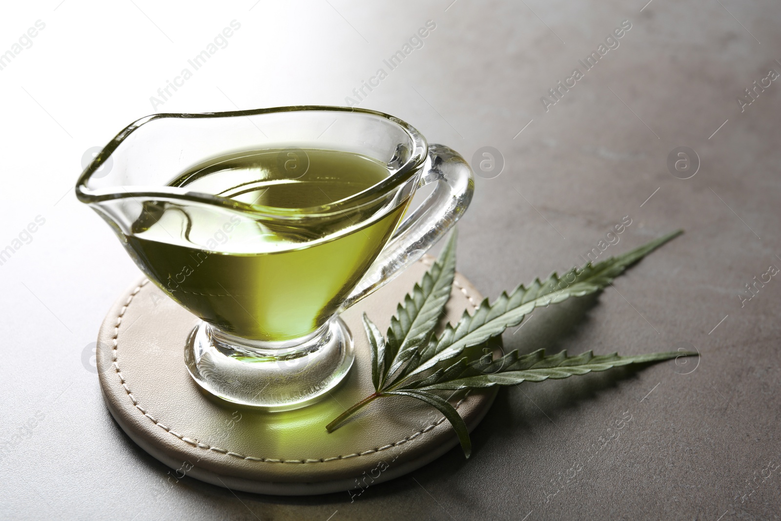 Photo of Gravy boat with hemp oil and leaf on gray table