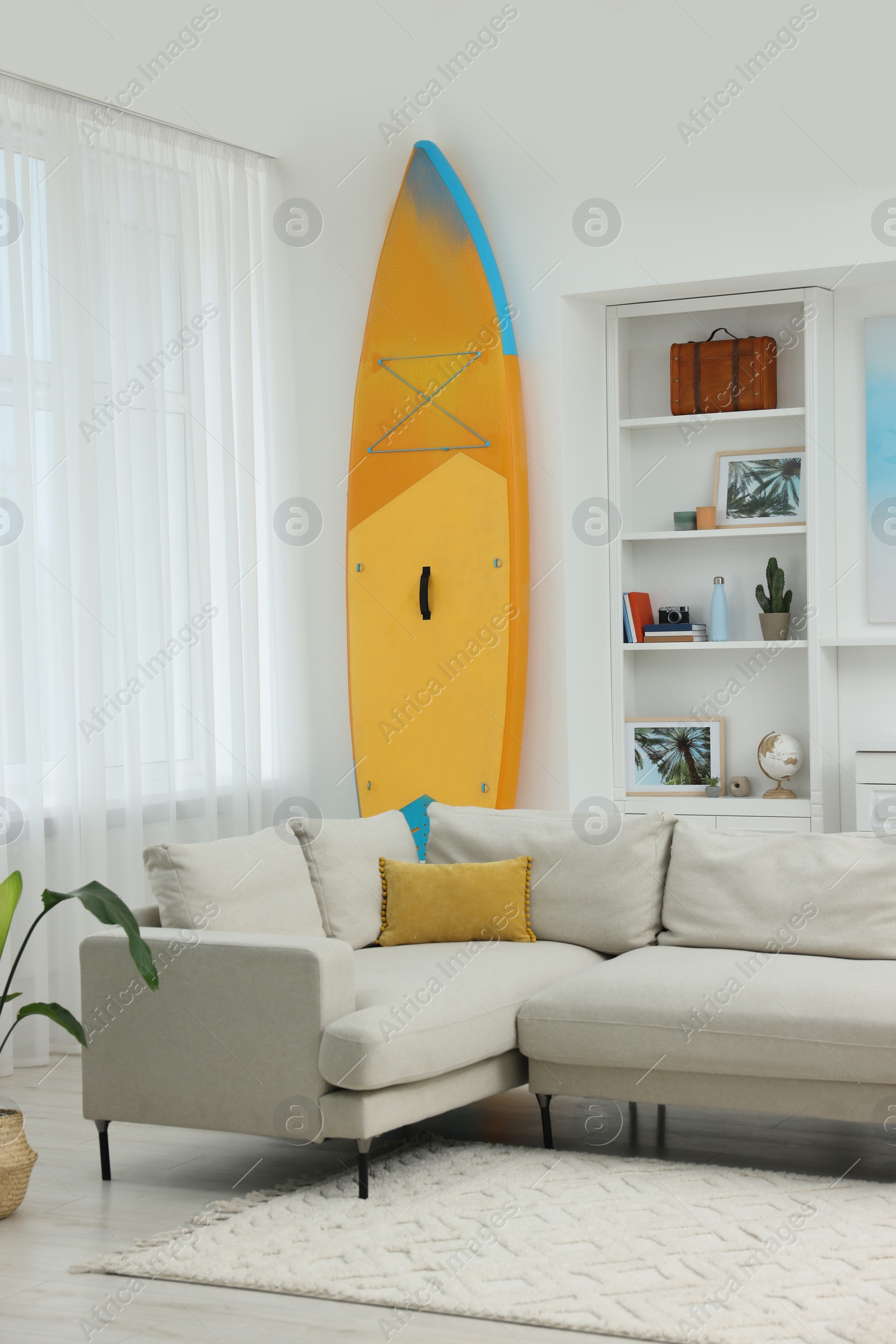 Photo of SUP board, shelving unit with different decor elements and stylish sofa in room. Interior design