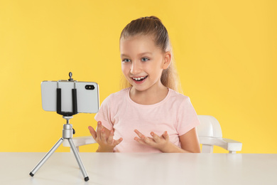 Cute little blogger recording video at table on yellow background