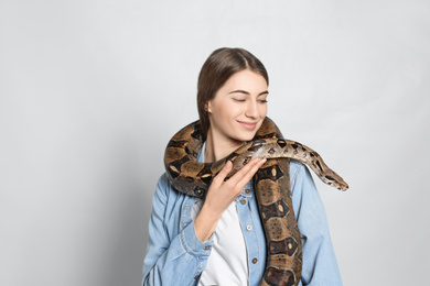 Photo of Young woman with boa constrictor on light background. Exotic pet