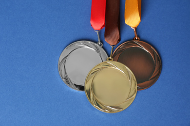 Photo of Gold, silver and bronze medals on blue background, flat lay. Space for design