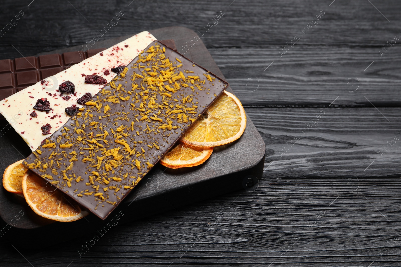 Photo of Board and different chocolate bars with freeze dried fruits on black wooden table. Space for text