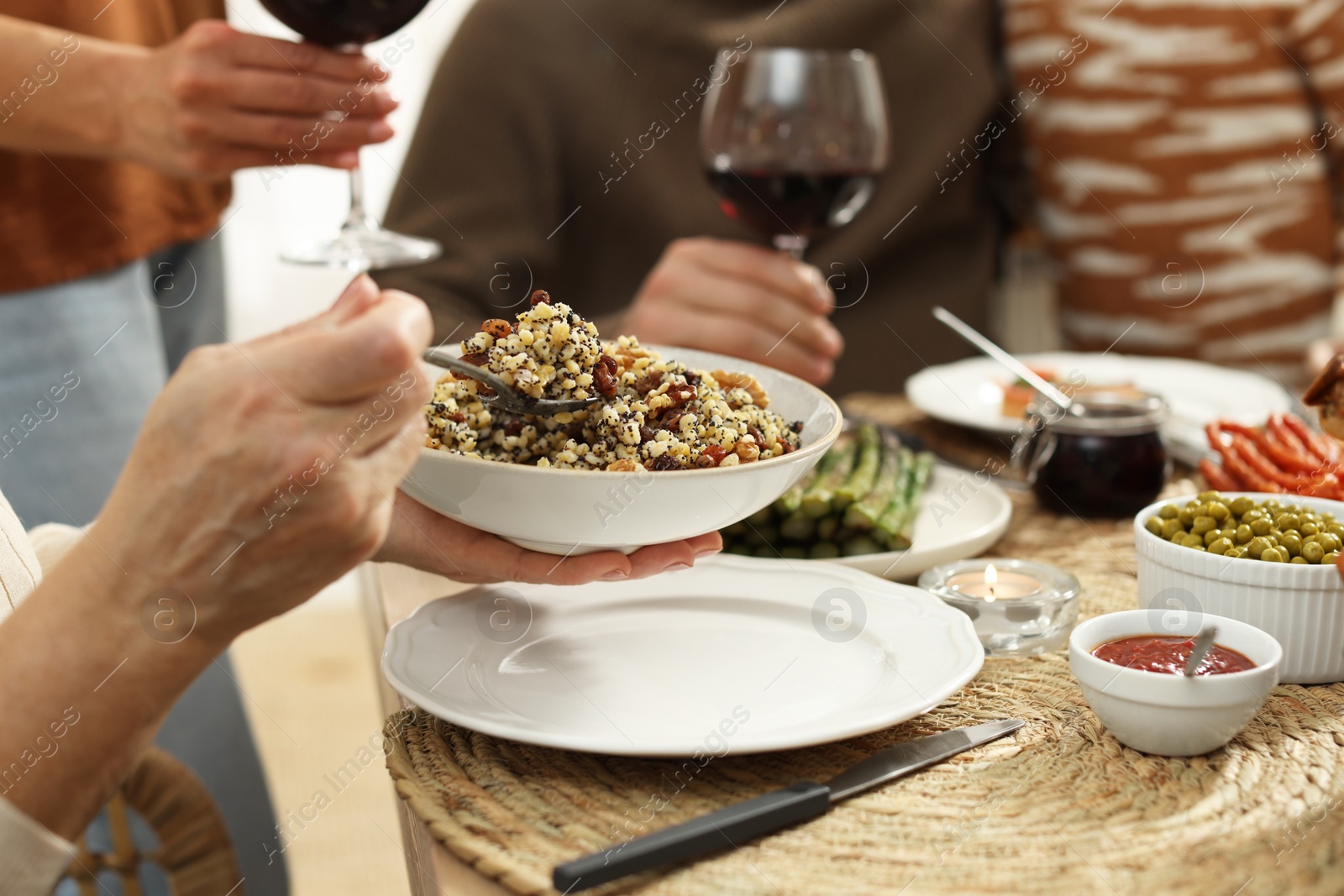 Photo of Woman with bowl of traditional Christmas kutia and her family at festive dinner, closeup. Slavic dish