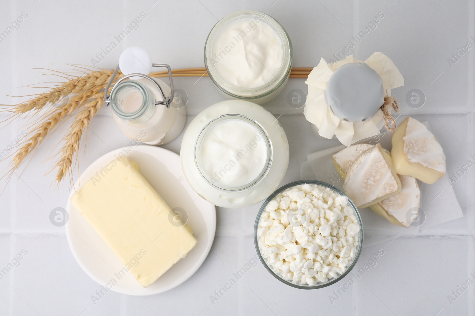 Photo of Different dairy products and spikes on white tiled table, flat lay