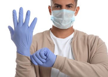 Man in protective face mask putting on medical gloves against white background, closeup